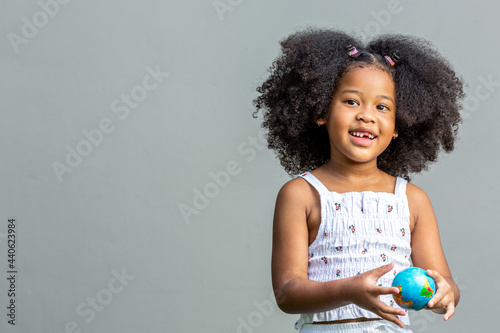 Child, woman, afro hairstyle holding a mock globe in hand showing emotions and poses. Isolated on gray background, childhood, and emotion concept.