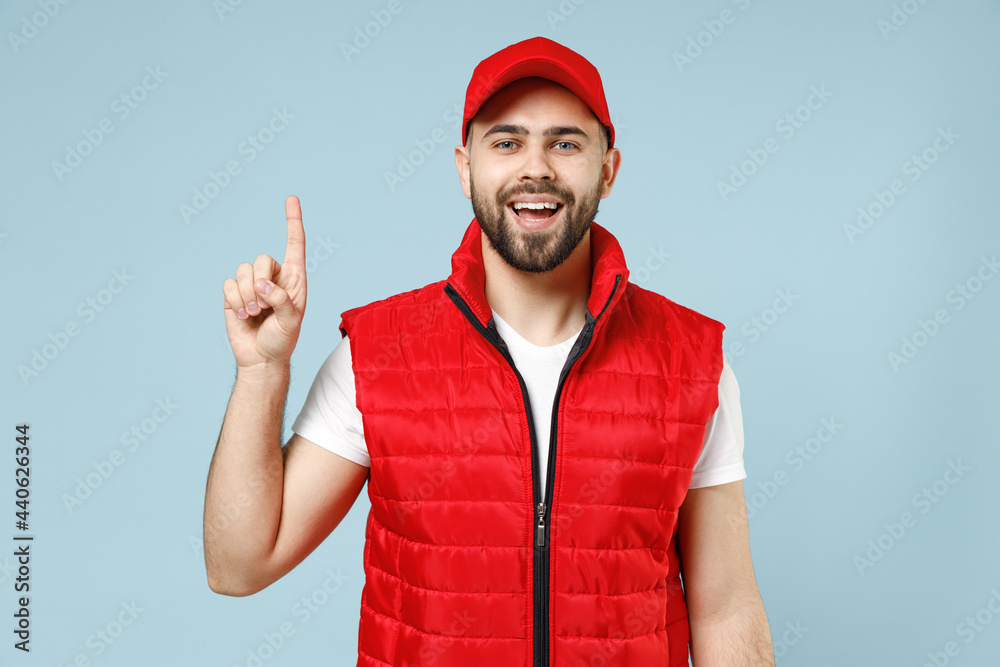 Professional delivery guy employee man in red cap white T-shirt vest uniform workwear work as dealer courier raised finger up isolated on pastel blue color background studio portrait. Service concept. Professional delivery guy employee man in red cap white T-shirt vest uniform workwear work as dealer courier raised finger up isolated on pastel blue color background studio portrait. Service concept.