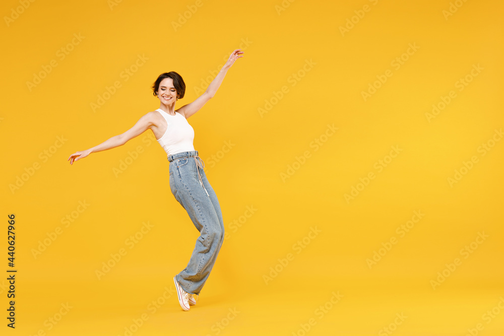 Full length side view young woman 20s with bob haircut wearing white tank top shirt walking go stand on toes leaning back fooling around dancing isolated on yellow background People lifestyle concept.