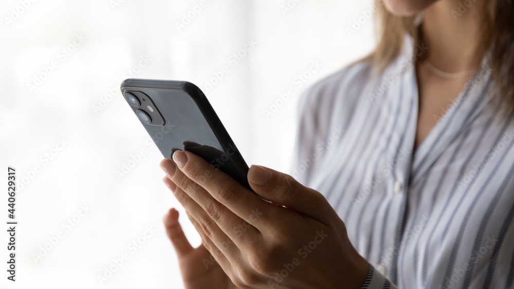 Close up unrecognizable young woman holding cellphone in hands, communicating distantly with friends, choosing goods in internet store, shopping online, web surfing information or playing game.