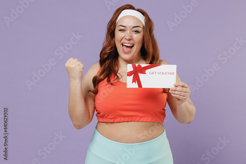 Young chubby plus size big fat fit woman in red top warm up training hold gift certificate coupon voucher card winner gesture isolated on purple background home gym Workout sport motivation concept photo