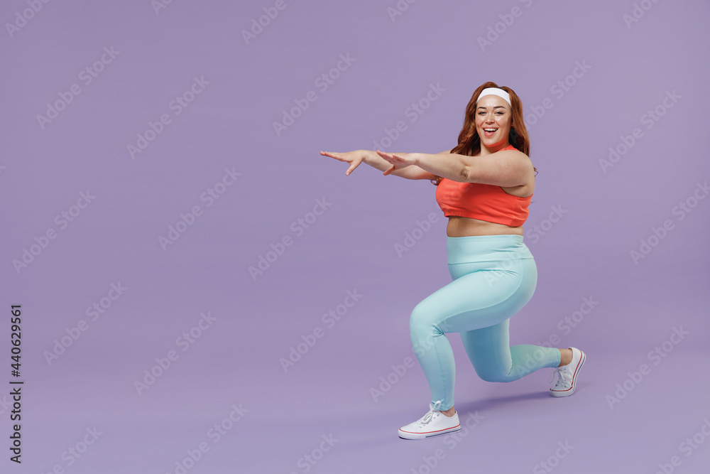 Full length side view young chubby overweight plus size big fat fit woman in red top warm up train squating lunges with legs isolated on purple background home gym. Workout sport motivation concept.