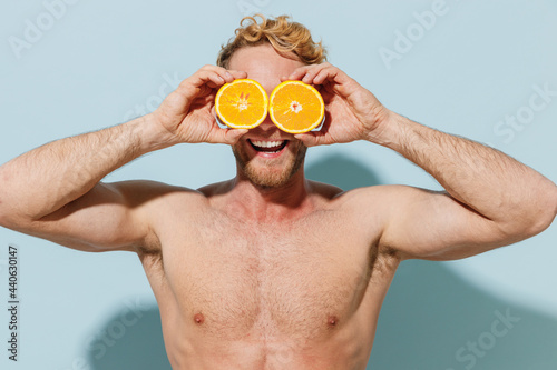 Handsome young fun man in red shorts swimsuit glasses relax near hotel pool cover eye with orange citrus fruits isolated on pastel blue background Summer vacation sea sun tan vegeterian food concept. photo