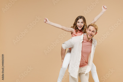 Young parent man have fun with child teen girl incasual pastel clothes Dad little kid daughter giving piggyback ride to joyful, sit on back do flying gesture clench fist isolated on beige background. photo