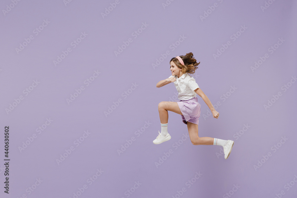 Full length side view of little fun overjoyed kid girl 12-13 years old in white short sleeve shirt jumping high run fast hurrying up isolated on purple background Childhood children lifestyle concept