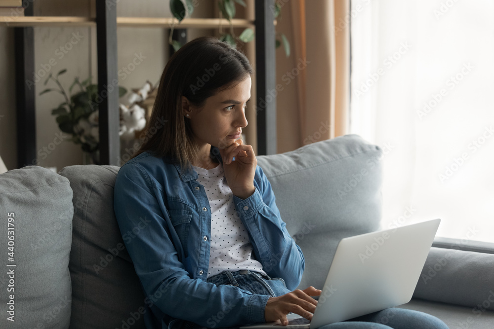 Thoughtful distracted young woman sitting on sofa with computer on laps, looking in distance considering problems or pondering tasks, waiting for message or email, doing remote freelance work at home. Thoughtful distracted young woman sitting on sofa with computer on laps, looking in distance considering problems or pondering tasks, waiting for message or email, doing remote freelance work at home.