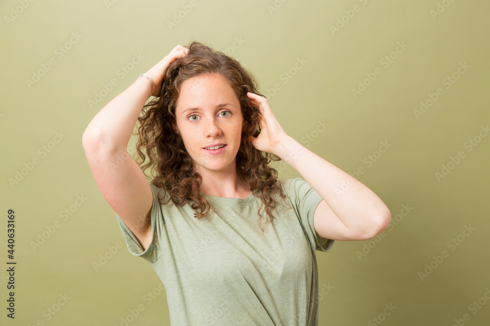 portrait pretty redhead smiling girl with hands in hair looking at camera with green t-shirt and sort jeans on green background portrait pretty redhead smiling girl with hands in hair looking at camera with green t-shirt and sort jeans on green background