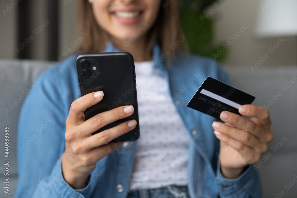 Close up cropped image sincere millennial generation woman holding credit card and cellphone in hands, transferring money in e-banking application, purchasing goods or service online, shopping concept Close up cropped image sincere millennial generation woman holding credit card and cellphone in hands, transferring money in e-banking application, purchasing goods or service online, shopping concept