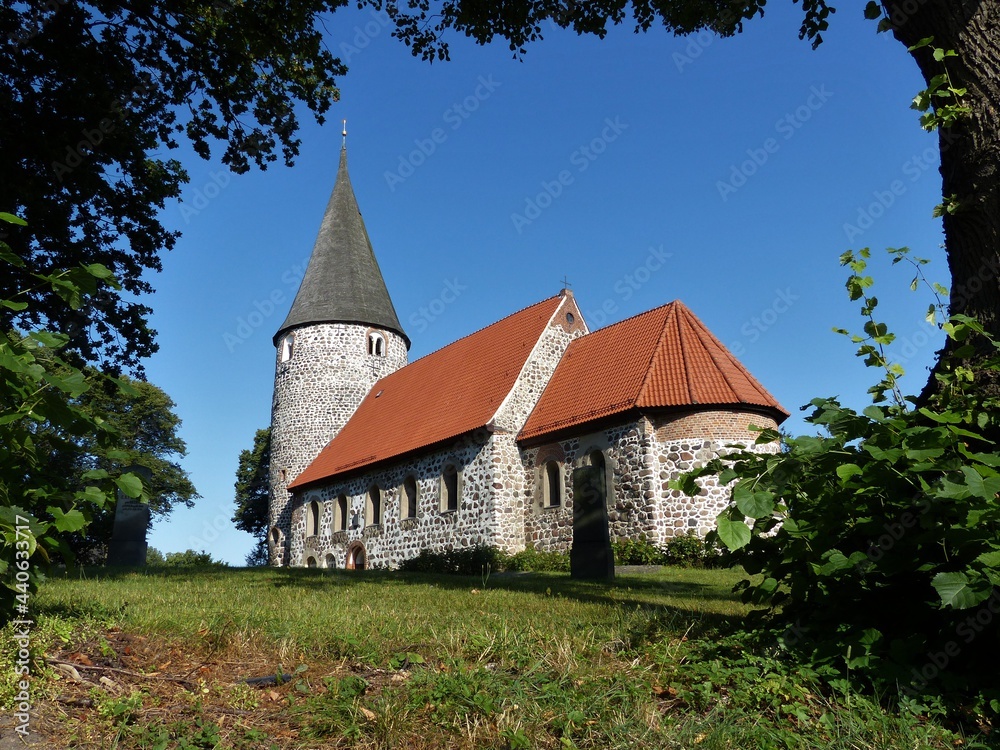 Feldsteinkirche eingerahmt von Baumzweigen auf grünem Rasen in Ratekau / Ostholstein