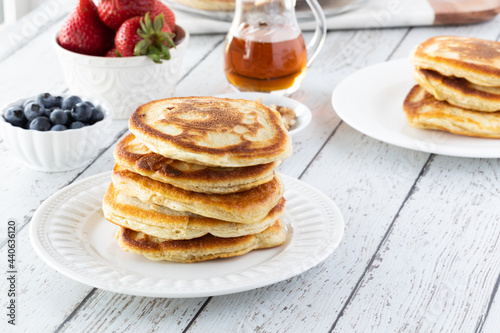 A fresh stack of warm buttermilk pancakes ready for toppings, on a light wooden table.