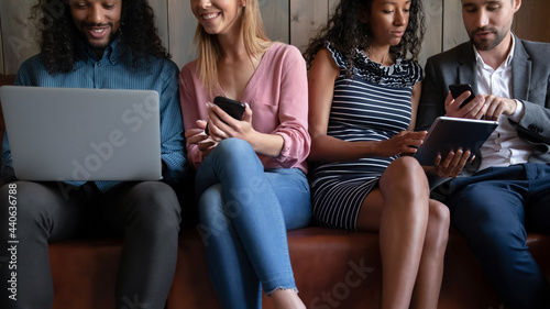 Cropped image young friendly multiracial people sitting on comfortable couch, involved in using different devices. Happy mixed race friends sharing applications or funny information, tech addiction.