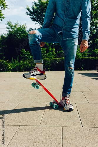 Young guy in ripped jeans standing with penny board in the park. summer activities skateboarding