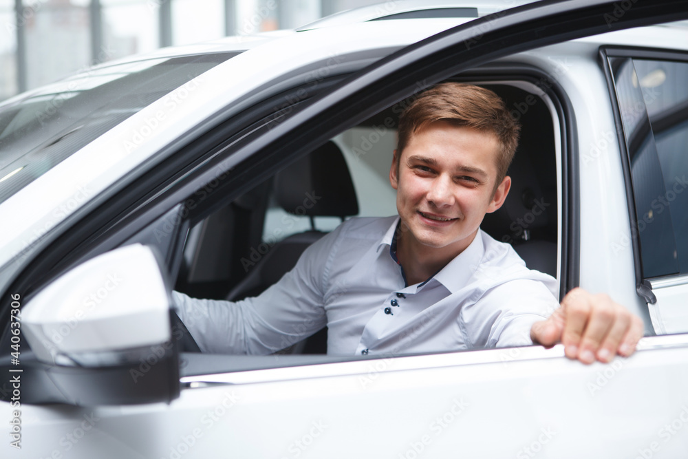 Excited young man smiling, choosing new automobile to buy at car dealership