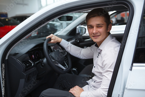 Young man choosing new car to buy at dealership salon, sitting in a new auto © Ihor