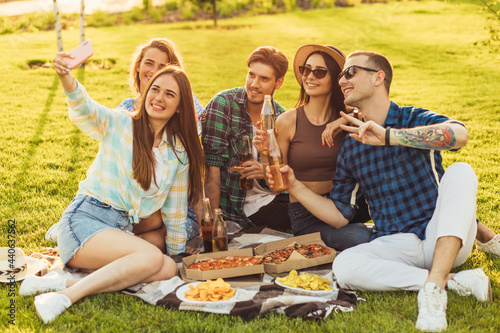 Obraz na płótnie Group of young people taking selfie while eating pizza, friends are sitting around during an outdoor party on the grass w salonie