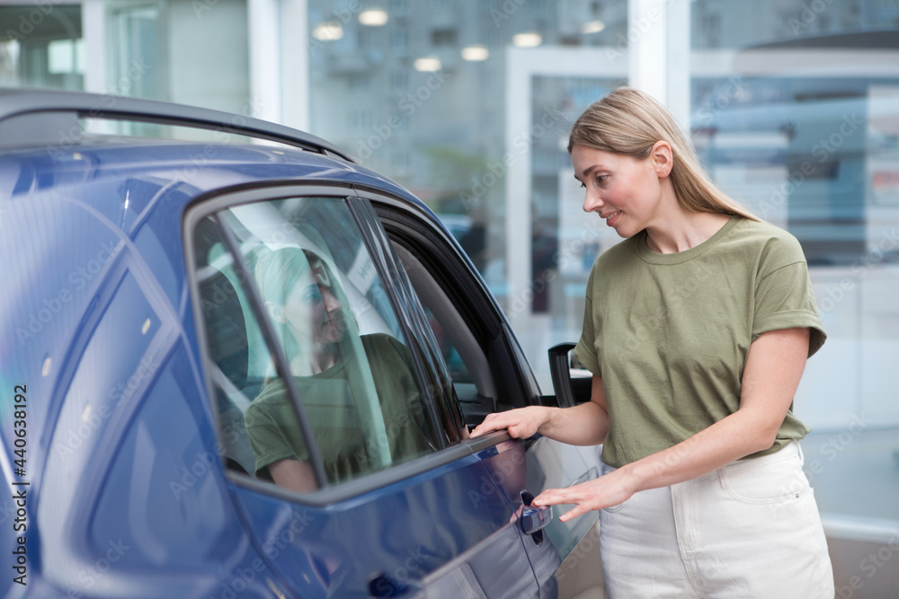 Female customer examining auto for sale at car dealership Female customer examining auto for sale at car dealership