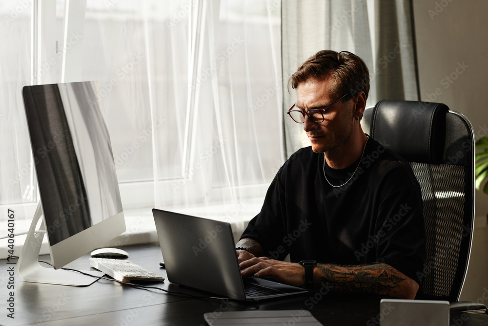 Serious programmer working on laptop at the table and developing new software at developing company