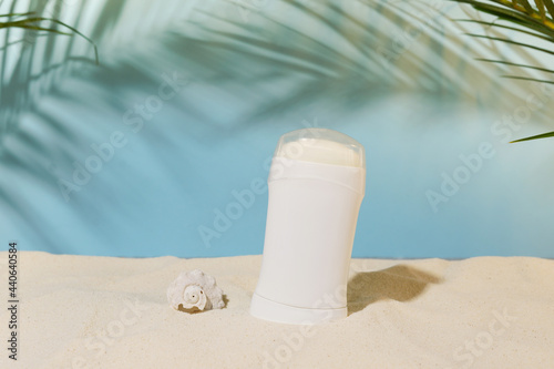 white deodorant or antiperspirant on summer sunny background with sand on the beach by the sea, green palm leaves