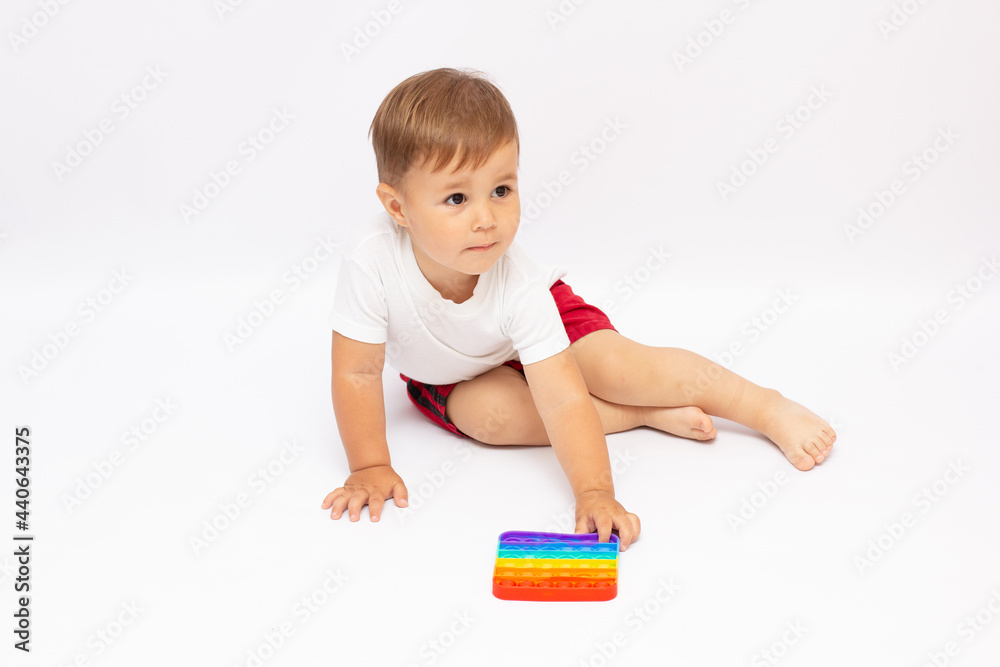 anti stress sensory pop it toys in a children's hands. a little happy kid boy plays with a simple dimple toy at home. toddler holding and playing popit rainbow hue bright color, trend 2021 year anti stress sensory pop it toys in a children's hands. a little happy kid boy plays with a simple dimple toy at home. toddler holding and playing popit rainbow hue bright color, trend 2021 year