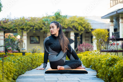 Beautiful yogi girl in black sports wear practicing yoga, sporty young girl sitting in matsyendrasana pose, exercising in garden.
 photo