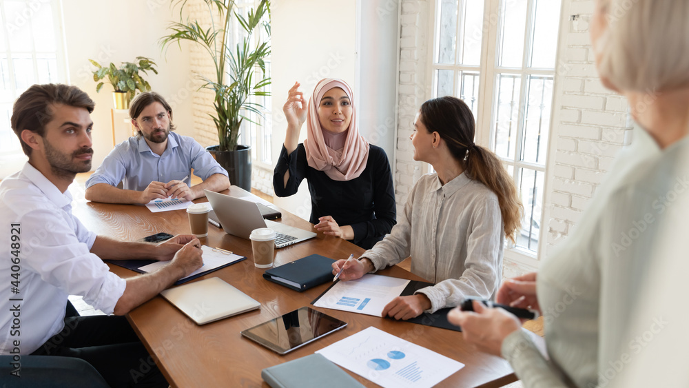 Curious Asian muslim businesswoman with raised hand asking question to business coach mentor at meeting, confident female voting as volunteer at seminar, diverse employees team discussing strategy Curious Asian muslim businesswoman with raised hand asking question to business coach mentor at meeting, confident female voting as volunteer at seminar, diverse employees team discussing strategy