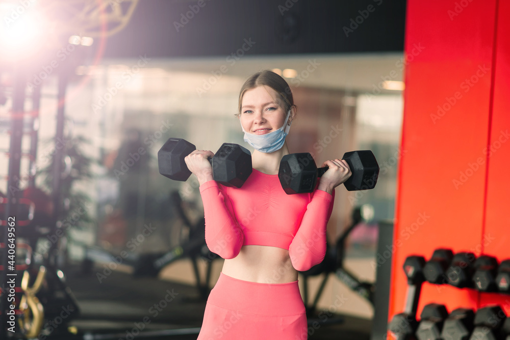 Coronavirus covid-19 prevention, fitness girl with medical mask holding a dumbbell, training circuit