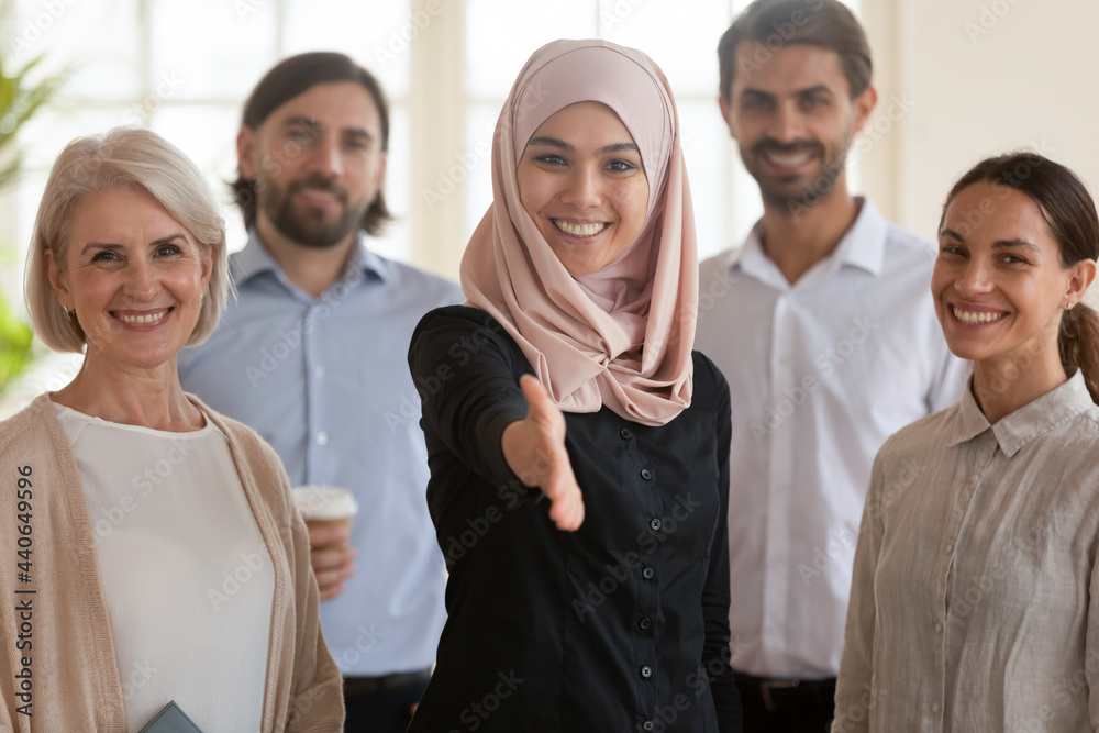 Smiling Asian muslim businesswoman team leader standing with extended hand for handshake, offering job, happy multiethnic employees group business people with executive posing for photo in office