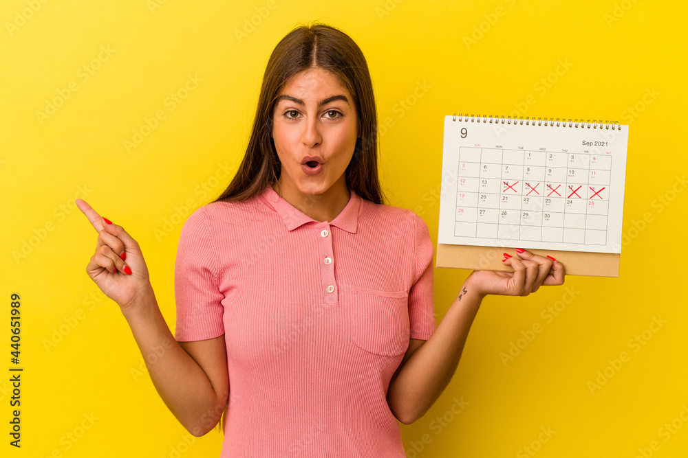 Young caucasian woman holding a calendar isolated on yellow background pointing to the side Young caucasian woman holding a calendar isolated on yellow background pointing to the side