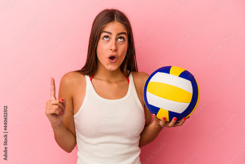 Young caucasian woman holding a volleyball ball isolated on pink background pointing upside with opened mouth.