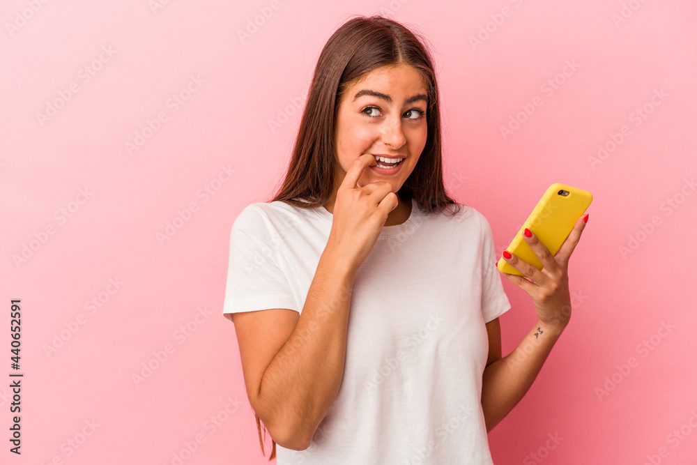 Young caucasian woman holding a mobile phone isolated on pink background relaxed thinking about something looking at a copy space. Young caucasian woman holding a mobile phone isolated on pink background relaxed thinking about something looking at a copy space.