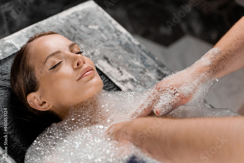 Close-up portrait of girl on foam peeling procedures in spa. Model is relaxing in Turkish hammam.