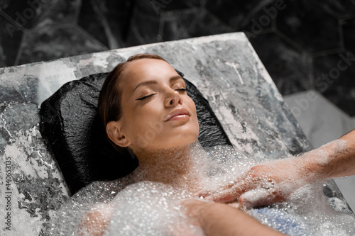 Close-up portrait of girl on foam peeling procedures in spa. Model is relaxing in Turkish hammam.