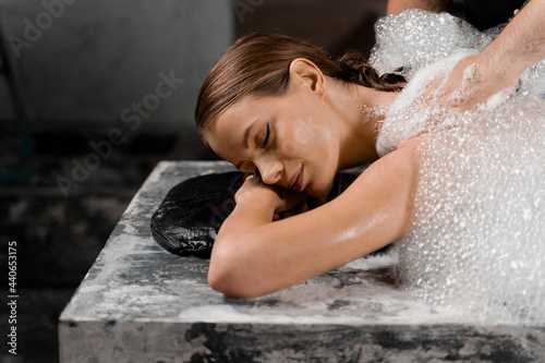Attractive girl relaxing in spa. Masseur is making foam peeling in Turkish spa hammam.