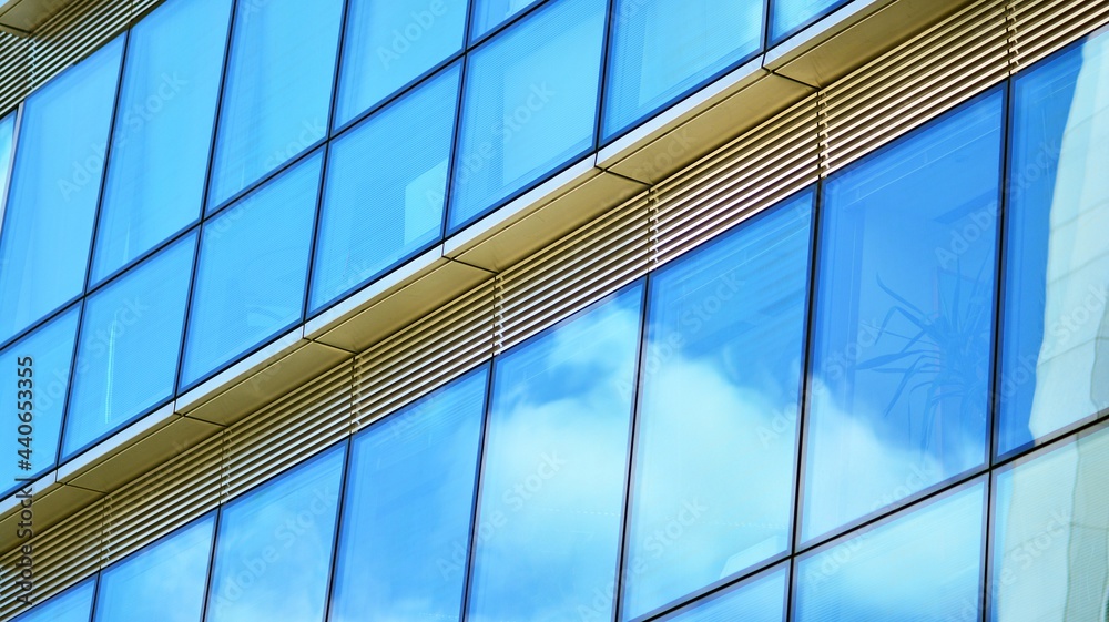 Obraz premium Abstract closeup of the glass-clad facade of a modern building covered in reflective plate glass. Architecture abstract background. Glass wall and facade detail.