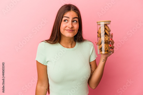Foto Young caucasian woman holding a cookies jar isolated on pink background dreaming