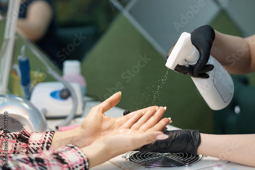 cosmetologist in the beauty salon treats the patient's hands with antiseptic, water spray, hygiene