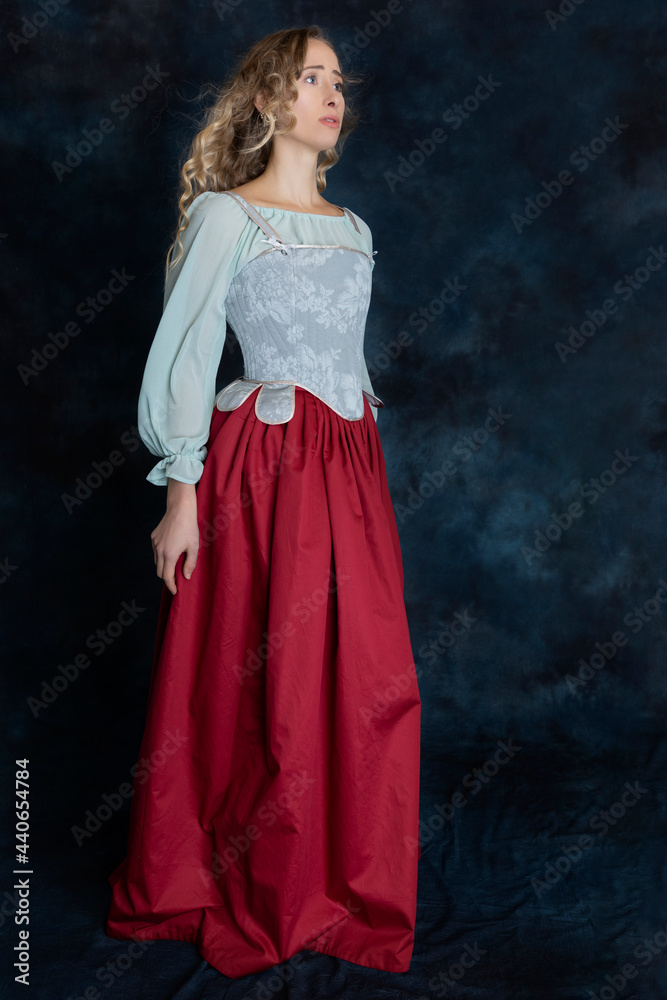 A Renaissance or Georgian woman wearing a brocade corset and red skirt against a studio backdrop A Renaissance or Georgian woman wearing a brocade corset and red skirt against a studio backdrop