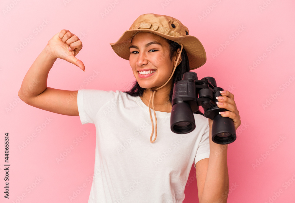Young mixed race explorer woman holding binoculars isolated on pink background feels proud and self confident, example to follow. Young mixed race explorer woman holding binoculars isolated on pink background feels proud and self confident, example to follow.