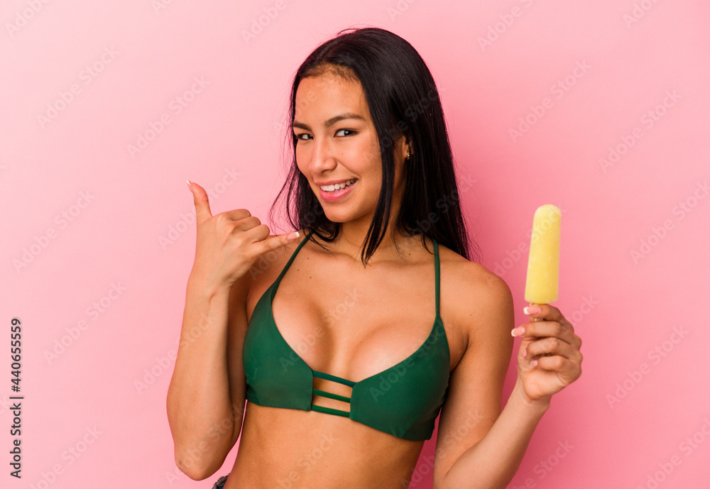 Young Venezuelan woman holding an ice cream isolated on pink background showing a mobile phone call gesture with fingers. Young Venezuelan woman holding an ice cream isolated on pink background showing a mobile phone call gesture with fingers.