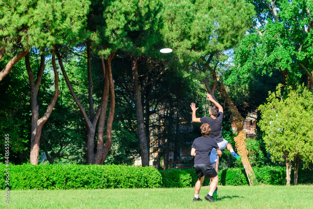 Group of mixed young teenagers people in casual wear playing with plastic flying disc game in a park oudoors. jumping man catch a disk to a teammate in a match. milennials friends outside in a garden
