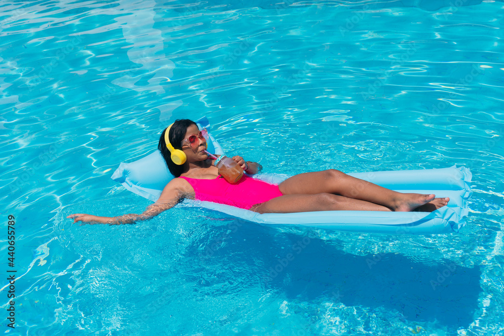 African American Woman sunbathing drinking a juice in a swimming pool
