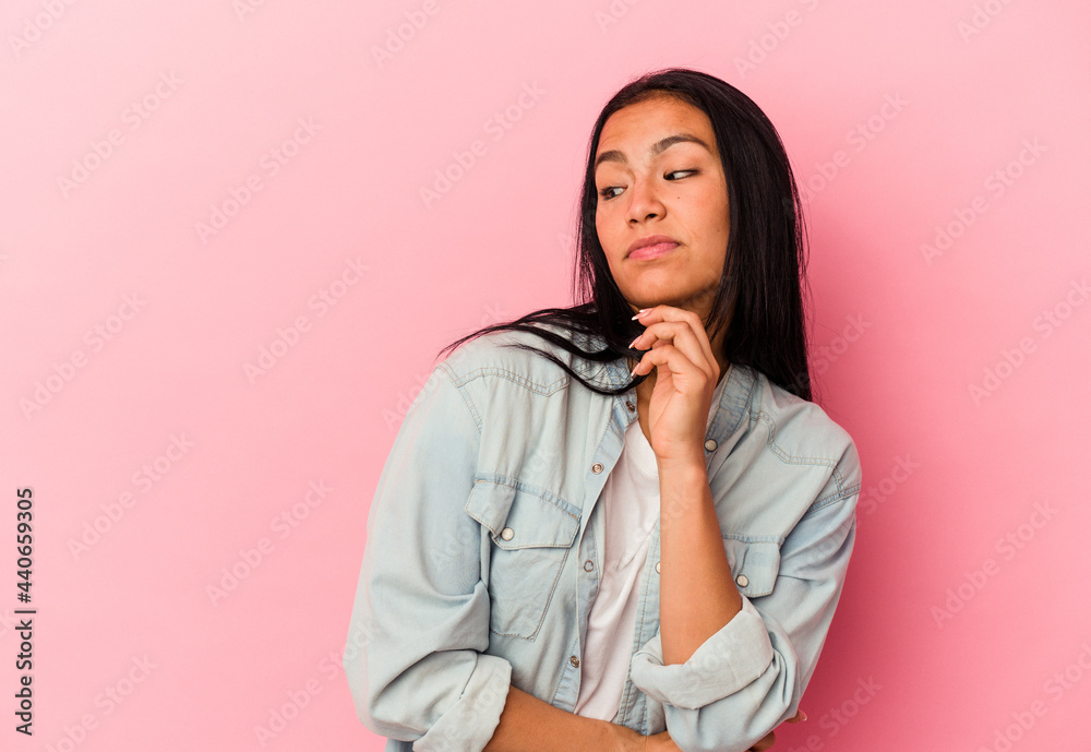 Young Venezuelan woman isolated on pink background confused, feels doubtful and unsure.