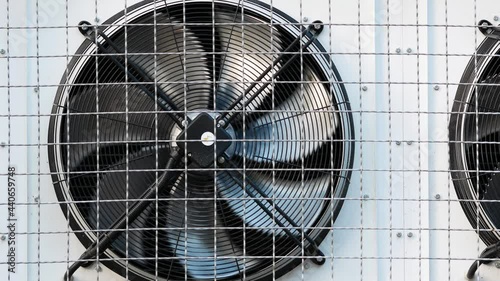 Industrial refrigeration unit mounted on wall of warehouse building. Unit with external cooling fans. Rotating blades. Metal turbine. Air conditioning equipment. Protective steel grill. Freezer unit