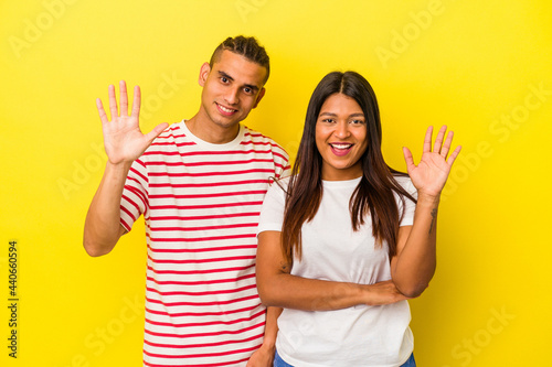 Young latin couple isolated on yellow background smiling cheerful showing number five with fingers.