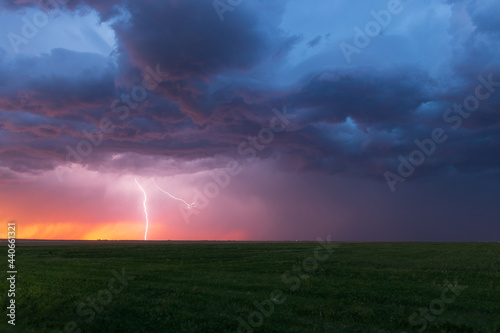 Lightning bolt strikes at dusk on the Wyoming / Colorado border with dark storm clouds overhead. The orange glow of sunset is seen on the horizon.