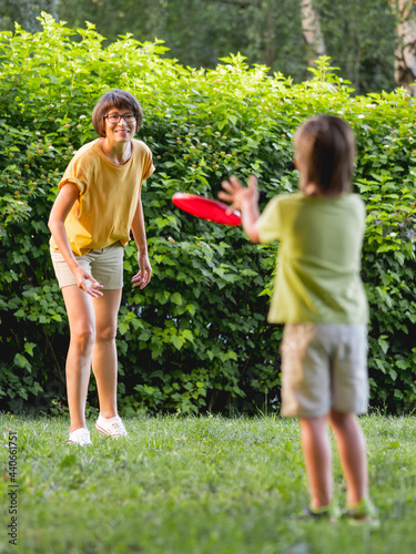 Mother and son play frisbee on grass lawn. Summer vibes. Outdoor leisure activity. Family life. Sports game at backyard.