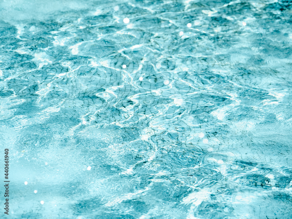 Sun beams on surface of water in swimming pool or fountain with blue mosaic bottom. Abstract background with wavy pattern of clear transparent water.