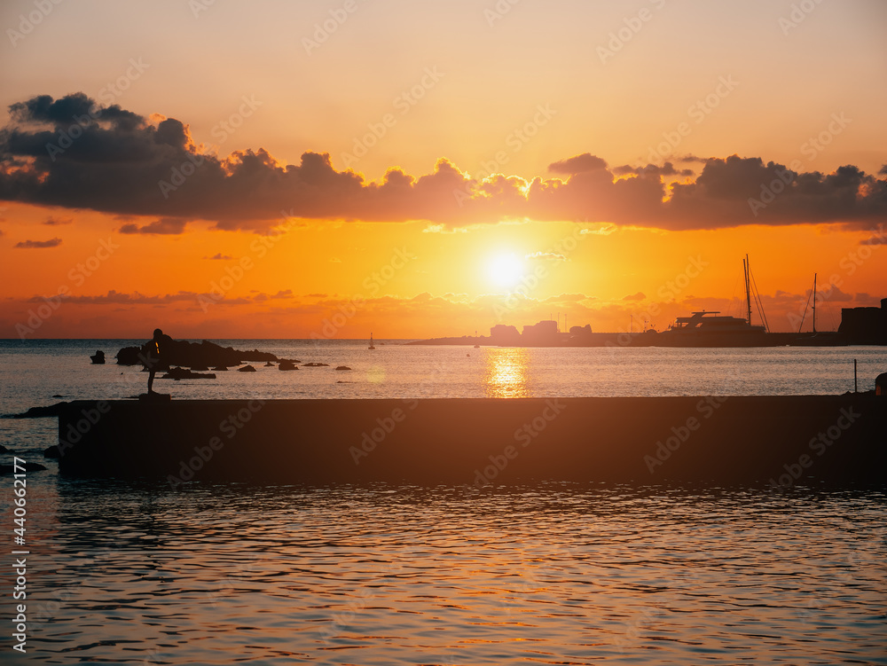 Tropical resort at beautiful colorful sunset over sea surface and silhouette of breakwater.
