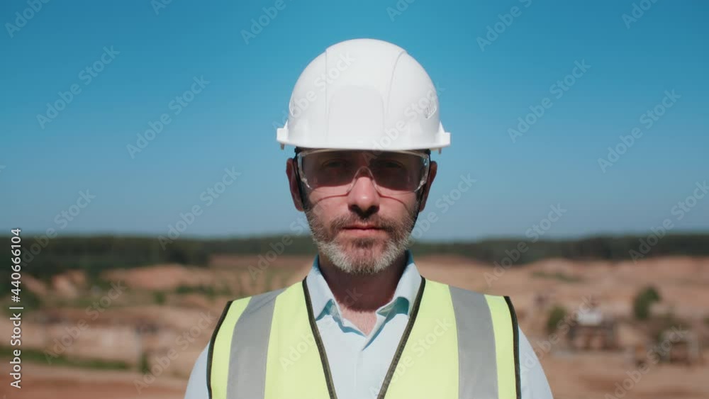 Portrait of handsome man sand quarry worker wearing safety uniform goggles and hard hat. Middle aged male bearded engineer looking at camera. Sand mining project professional on warm sunny day Portrait of handsome man sand quarry worker wearing safety uniform goggles and hard hat. Middle aged male bearded engineer looking at camera. Sand mining project professional on warm sunny day