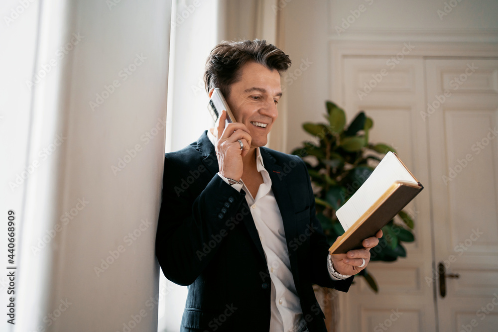 Fototapeta premium An adult male lawyer works in his office in a tablet and calls. Makes a design project remotely writes down new ideas in the diary. Dressed in a modern business suit.